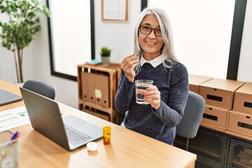 Obraz premium Middle age grey-haired woman business worker taking pills working at office