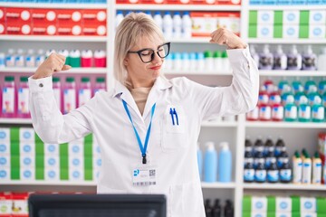 Young caucasian woman working at pharmacy drugstore showing arms muscles smiling proud. fitness...