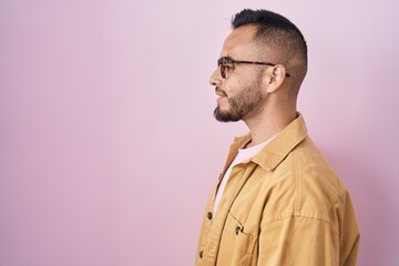 Young hispanic man standing over pink background looking to side, relax profile pose with natural face with confident smile.