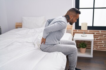 Fototapeta premium Young hispanic man suffering for backache sitting on bed at bedroom