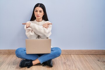 Young woman using laptop sitting on the floor at home pointing to both sides with fingers, different direction disagree