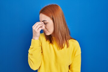 Young woman standing over blue background tired rubbing nose and eyes feeling fatigue and headache. stress and frustration concept.