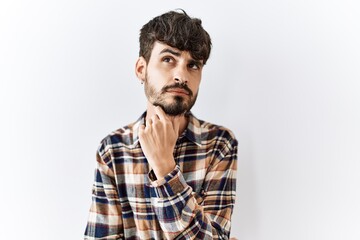 Obraz premium Hispanic man with beard standing over isolated background with hand on chin thinking about question, pensive expression. smiling with thoughtful face. doubt concept.