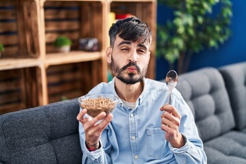 Young hispanic man with beard eating healthy whole grain cereals looking at the camera blowing a kiss being lovely and sexy. love expression.