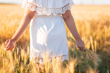 Young girl walking through field and touches wheat.