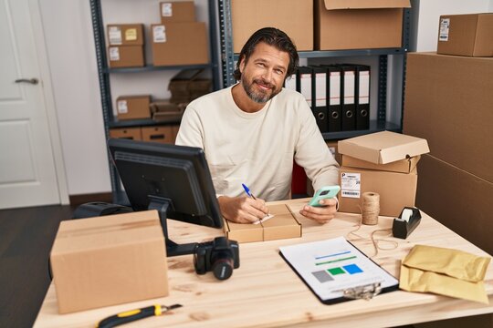 Middle age man ecommerce business worker using smartphone writing on package at office