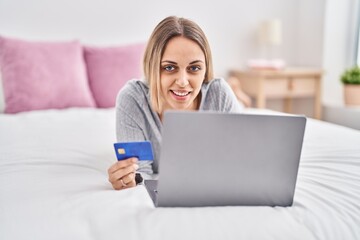 Young woman using laptop and credit card lying on bed at bedroom