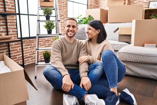 Man and woman couple hugging each other sitting on floor at new home