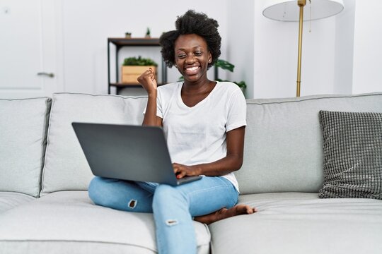 African young woman using laptop at home screaming proud, celebrating victory and success very excited with raised arm
