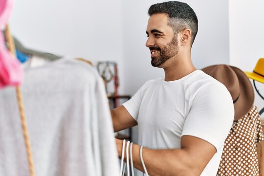 Young hispanic man customer choosing clothes shopping at clothing store