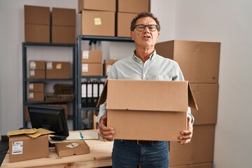 Senior man working at small business ecommerce holding carboard bx looking at the camera blowing a kiss being lovely and sexy. love expression.