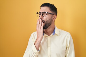 Hispanic young man wearing business clothes and glasses bored yawning tired covering mouth with hand. restless and sleepiness.