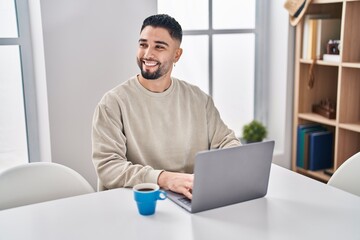 Young arab man using laptop and drinking coffee sitting on table at home
