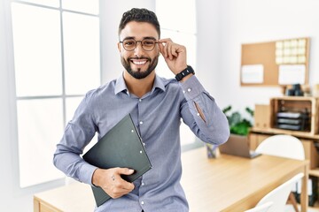 Young arab man smiling confident holding clipboard at office