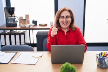 Obraz premium Senior woman with glasses working at the office with laptop smiling happy and positive, thumb up doing excellent and approval sign