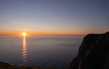 Wonderful landscapes in Norway. Nord-Norge. Beautiful scenery of a midnight sun sunset at Nordkapp (Cape North). Boat and globe on a cliff. Rippled sea and clear orange sky. Selective focus