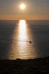 Wonderful landscapes in Norway. Nord-Norge. Beautiful scenery of a midnight sun sunset at Nordkapp (Cape North). Boat and globe on a cliff. Rippled sea and clear orange sky. Selective focus
