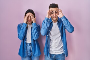 Young hispanic couple standing over pink background trying to open eyes with fingers, sleepy and tired for morning fatigue