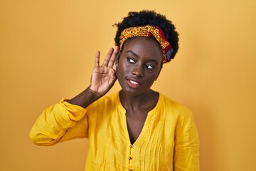Fototapeta premium African young woman wearing african turban smiling with hand over ear listening an hearing to rumor or gossip. deafness concept.