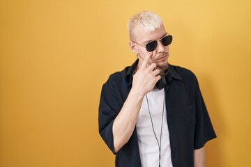 Fototapeta premium Young caucasian man wearing sunglasses standing over yellow background pointing to the eye watching you gesture, suspicious expression