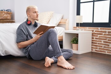 Young caucasian man reading book sitting on floor at bedroom