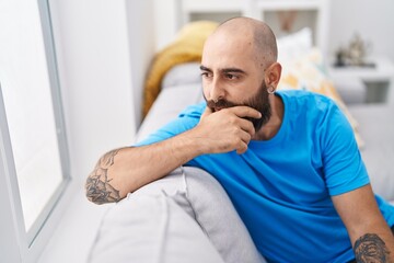 Young bald man sitting on sofa with serious expression at home