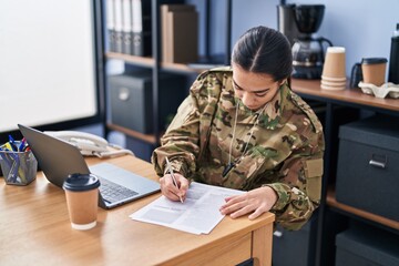 Young hispanic woman army soldier using laptop writing on document at office
