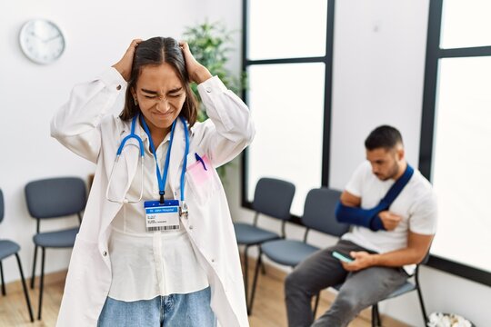 Young asian doctor woman at waiting room with a man with a broken arm suffering from headache desperate and stressed because pain and migraine. hands on head.