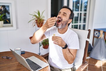Middle age man using laptop drinking medicine syrup at terrace home