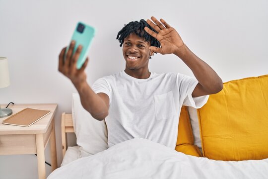 Young african man with dreadlocks taking a selfie on the bed looking positive and happy standing and smiling with a confident smile showing teeth