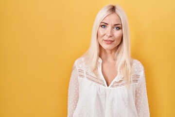 Caucasian woman standing over yellow background with serious expression on face. simple and natural looking at the camera.