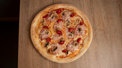 Italian pizza with cheese, ham, cherry tomatoes, onions and mushrooms on the table background