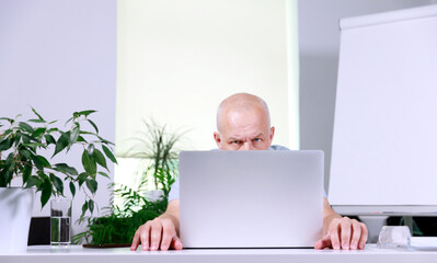 a gray-haired man with a very short haircut sits at a laptop and stares intently at the screen....