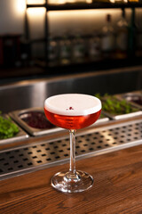 A glass of red alcohol drink with foam and flower petal. Cocktail garnish. Vertical orientation.