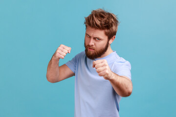 Portrait of bearded man standing with boxing fists and ready to attack or defence, looking with...