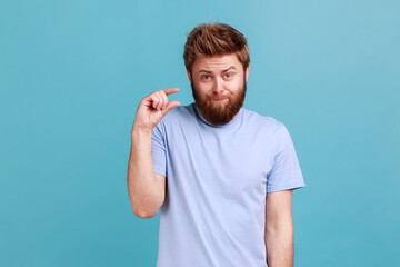 Portrait of disappointed bearded man showing a little bit gesture, dissatisfied with low rating,...