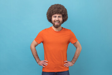 Portrait of cheerful man wearing orange T-shirt looking at camera with toothy smile and happy...