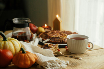 Atmospheric autumn still life. Warm tea in stylish cup on rustic wooden table with freshly baked apple pie with cinnamon, candle, autumn leaves, pumpkins and nuts. Hygge home, cozy moment