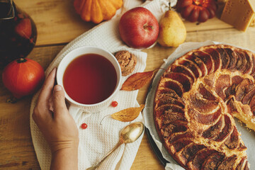 Hand holding warm tea in stylish cup on rustic wooden table with freshly baked apple pie with...