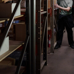 Unrecognizable person in light gray shirt stores a cardboard box in a warehouse. There are no trademarks in the shot.