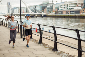 Two athletic women in sportswear are running along the embankment. Reaching the goal