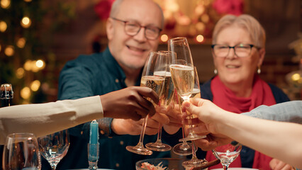 Festive family clinking champagne glasses while enjoying Christmas dinner at home. Happy diverse people celebrating winter feast while drinking sparkling wine together in ornate dining room.
