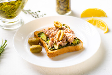 toast with tuna and avocado, olives with chimichurri sauce. On a white plate and white background.