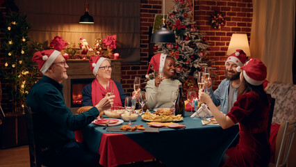 Happy family members wearing festive hats while clinking glasses with champagne. Joyful diverse...