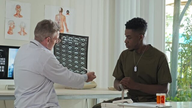 Caucasian doctor explaining x-ray image to African American military man during consultation in post war rehabilitation clinic