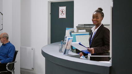 Portrait of african american receptionist working at registration desk in hospital waiting lobby....