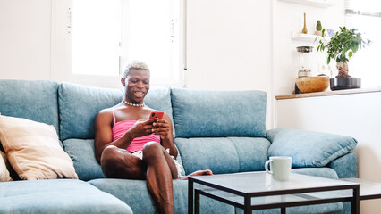 African Black transsexual man in stylish feminine clothes texting on cellphone on couch