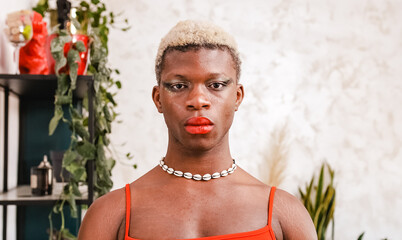 African black transgender model with stylish makeup looking at camera in daytime at home - obrazy, fototapety, plakaty