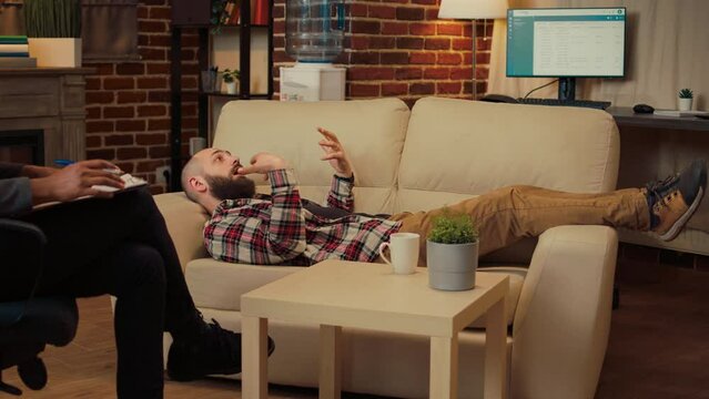Male therapist doing psychoanalysis with man laying on couch, talking about relationship and marriage problems. Attending therapy session with professional specialist, counseling advice.