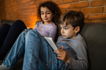 Small caucasian boy sitting by his sister using digital tablet at home